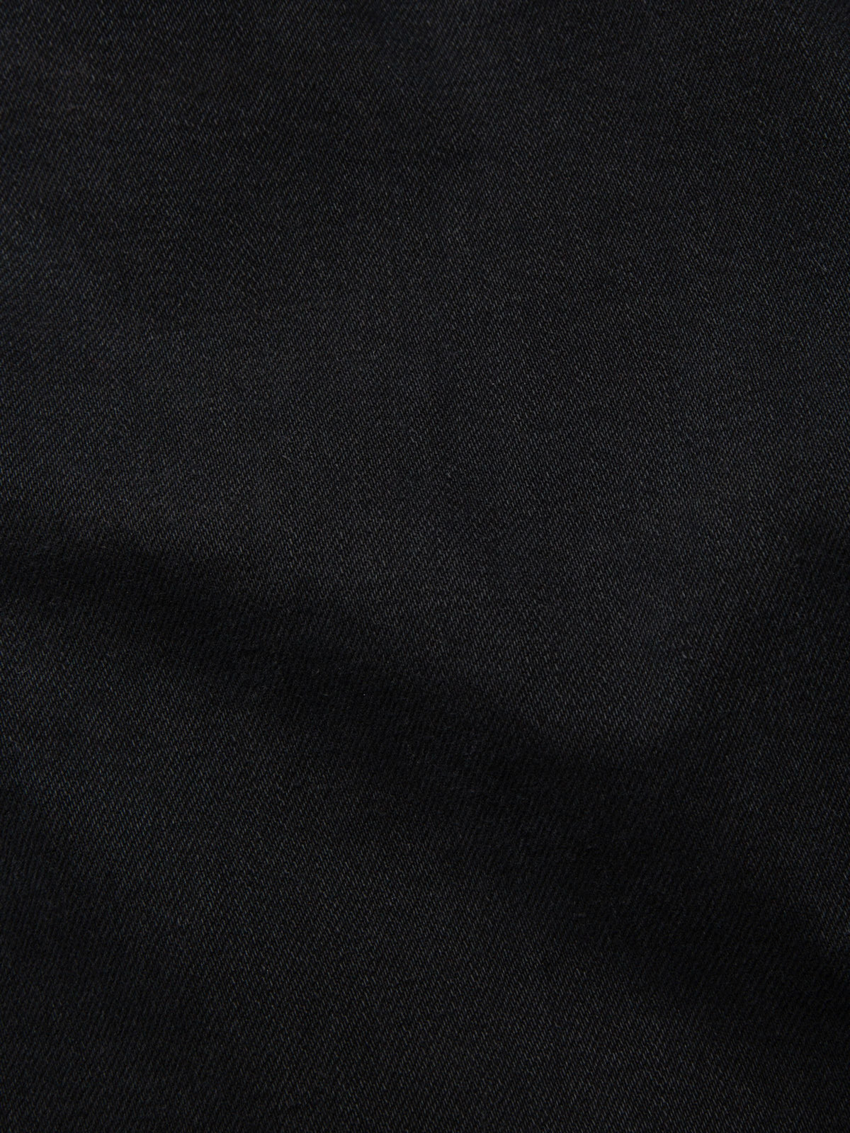 Nudie Jeans Gritty Jackson in Black Forest, a close-up showing the texture of the black rigid denim.