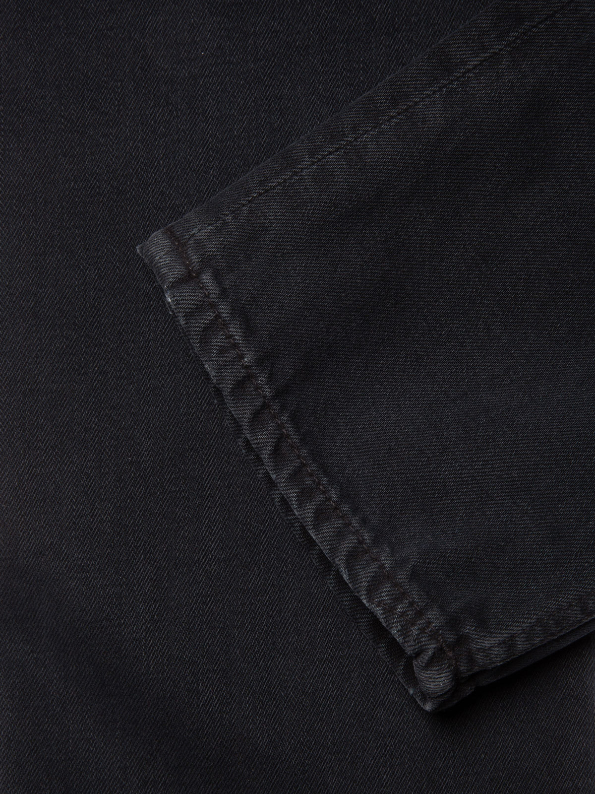 Nudie Jeans Gritty Jackson Black Forest, close-up of the leg opening showing the washed black rigid denim and hem.