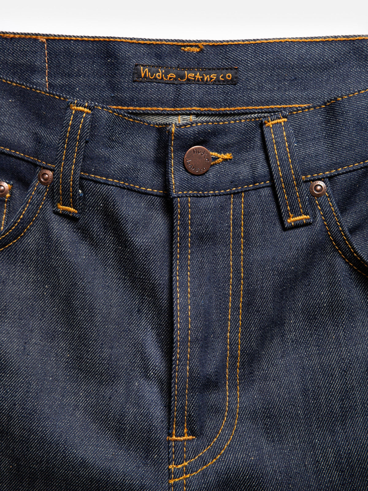 Nudie Jeans Gritty Jackson Dry Old, close-up of the zip fly, copper trims, tobacco stitching, and waistband brand logo.