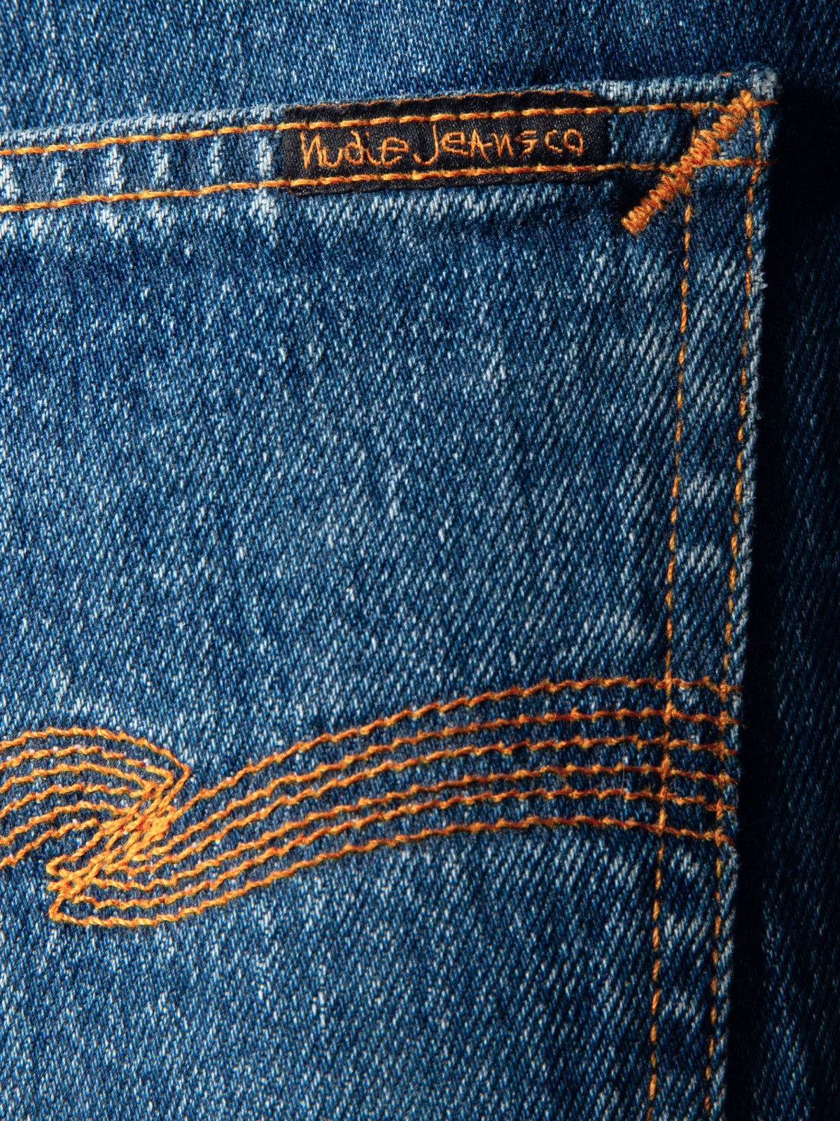 Nudie Jeans Solid Ollie Life Tracks, a close-up of the back pocket showing the orange thread embroidery and black logo tab.