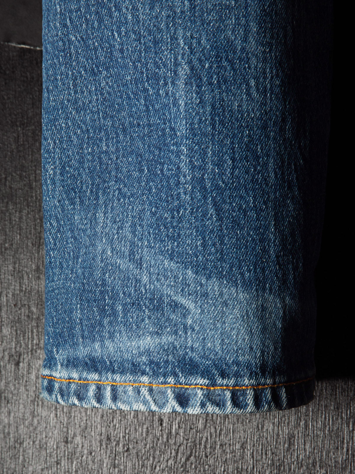 Nudie Jeans Solid Ollie Life Tracks, close-up of the hem showing orange stitching and wear on the mid-blue denim.